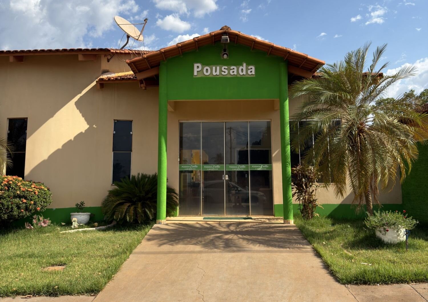 Entrada da Pousada Cantão: pórtico verde com a placa Pousada, porta de vidro, palmeira e jardim gramado