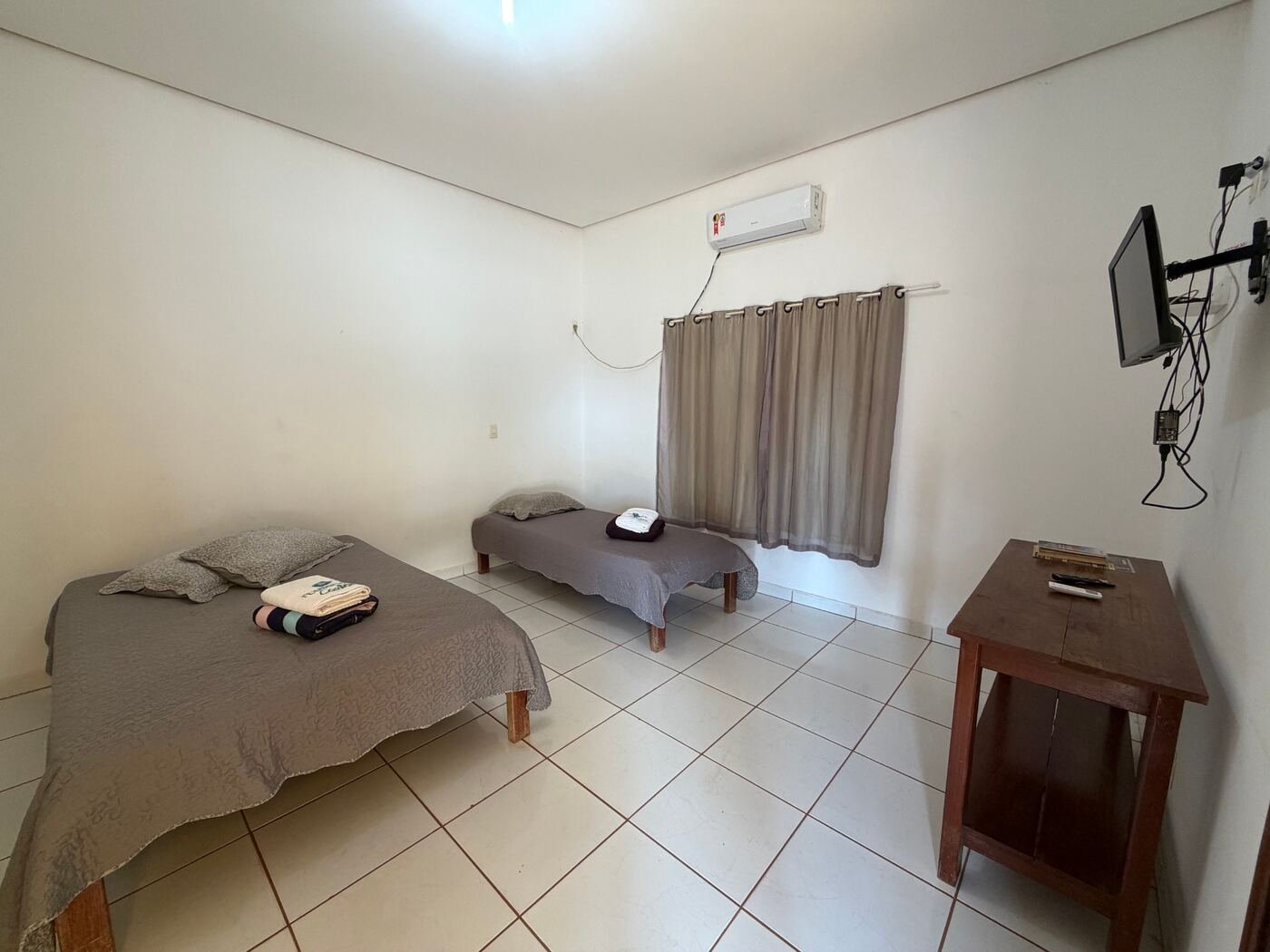 Quarto claro com cama de casal, cama de solteiro, ar-condicionado, TV e mesa de madeira