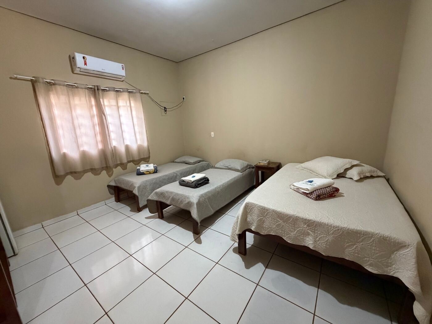 Quarto com cama de casal, duas camas de solteiro, ar-condicionado e toalhas sobre as camas