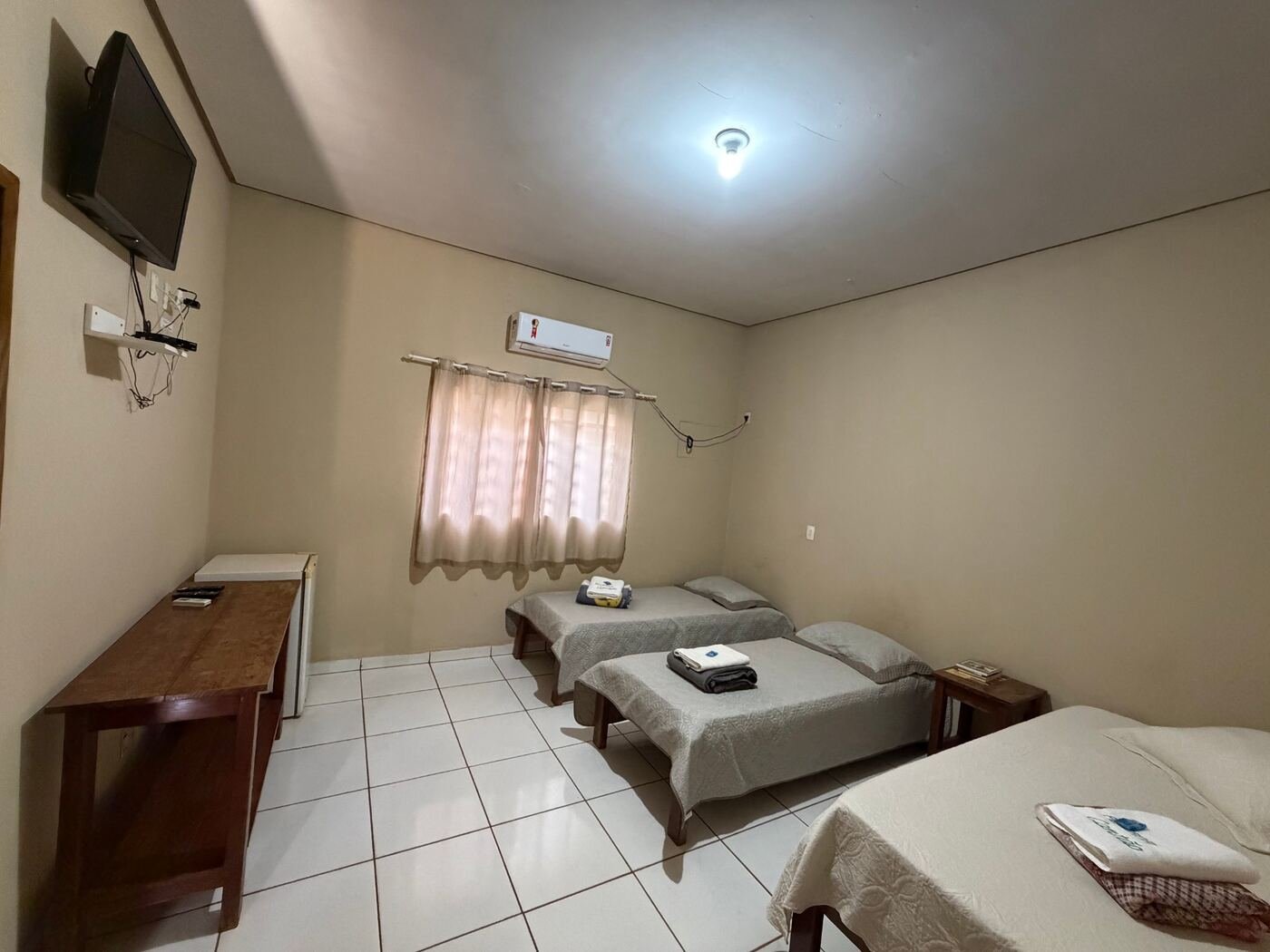 Quarto com TV na parede, ar-condicionado, frigobar, uma cama de casal e duas de solteiro